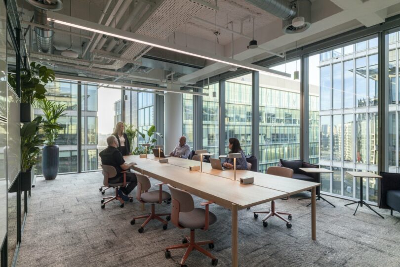 A meeting room with a wooden table, large windows, and lush green plants.