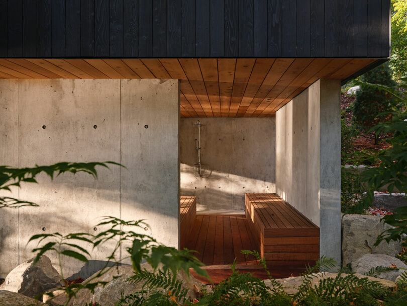 Modern outdoor space with concrete walls, wood ceiling, and an outdoor shower fixture set against rocks.