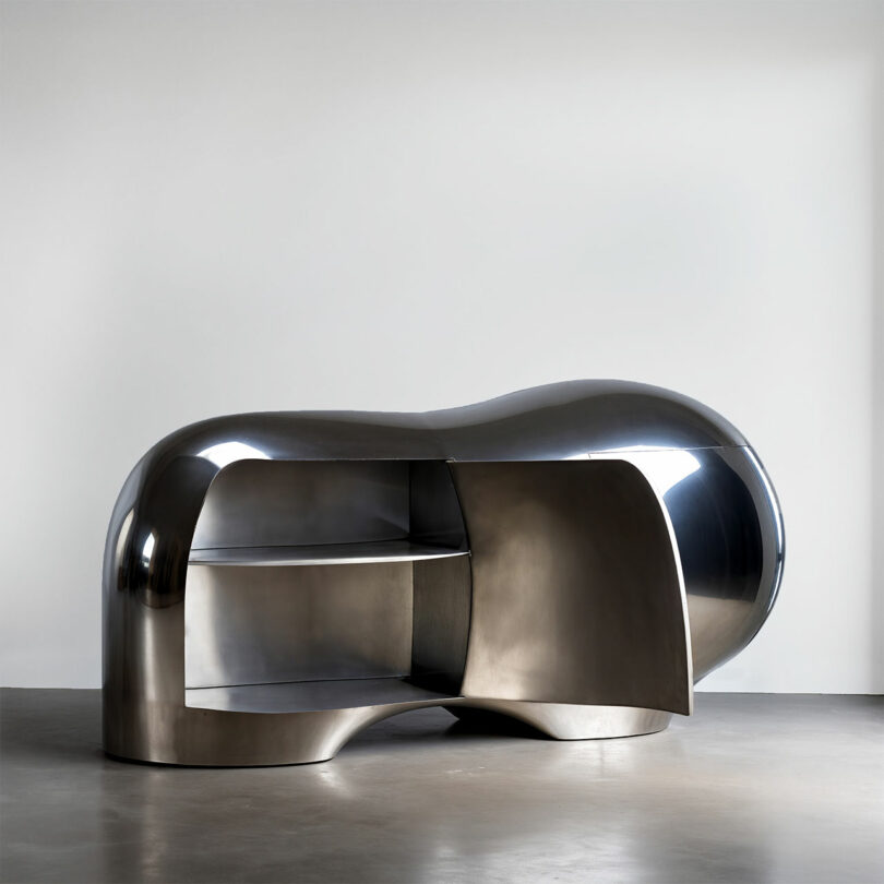A shiny, abstract-shaped chrome cabinet with open shelves and a partially open door.