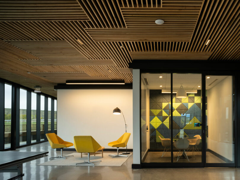 Modern office interior with yellow chairs and geometric acoustic panels on the wall under a wooden ceiling.