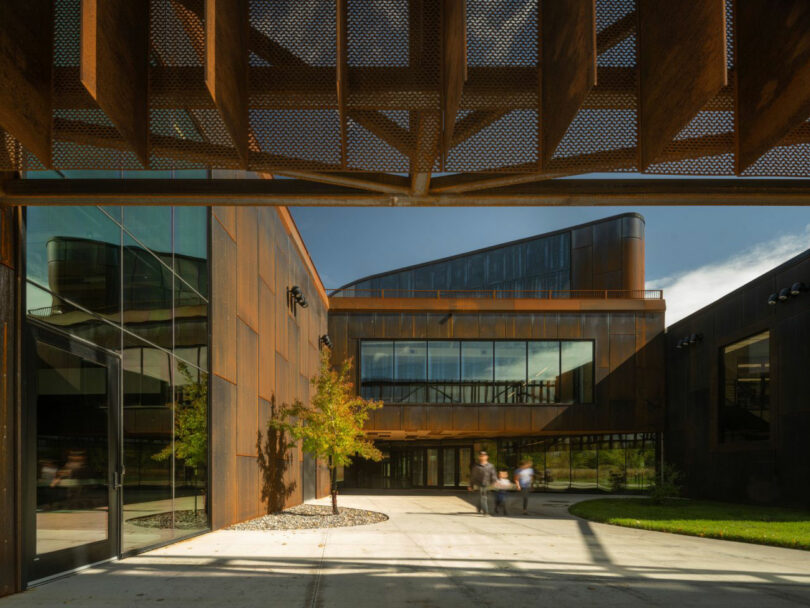 The rust-colored metal exterior of the EMIT Technologies building with large glass windows and a landscaped walkway.