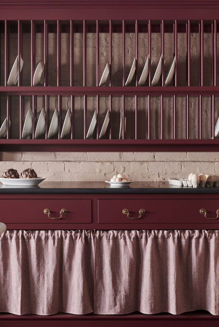 Traditional shaker-style kitchen cabinets in deep red with a matching plate rack and pale pinkish-beige walls.