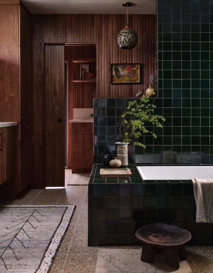 A modern bathroom featuring glossy green square tiles, walnut paneling, and terrazzo floor tiles.
