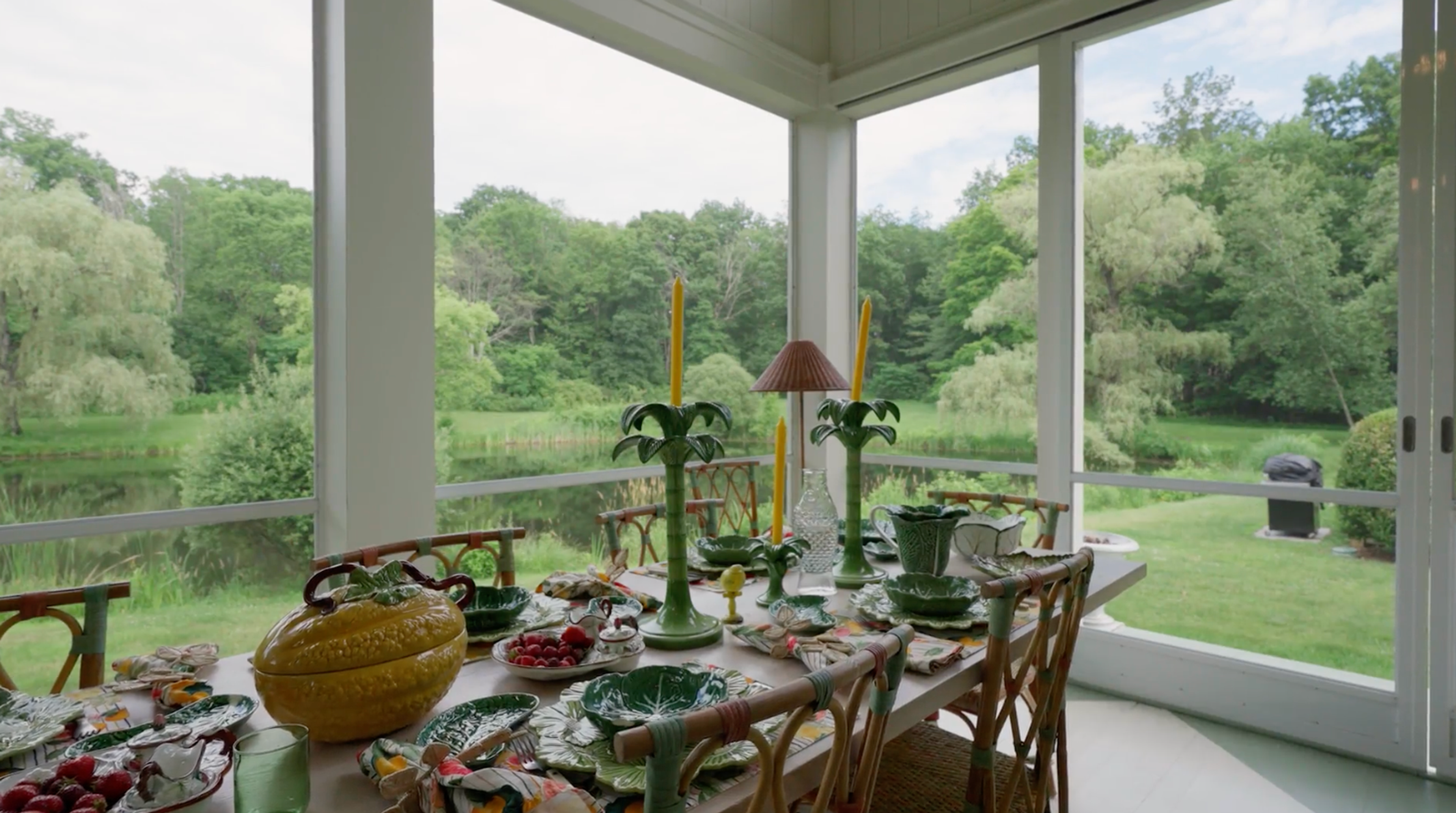 A long dining table set on a wooden porch with wicker chairs.
