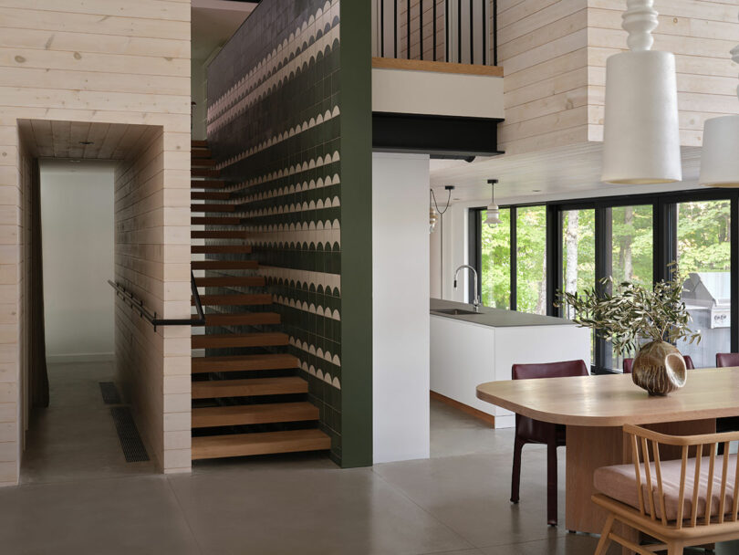 A minimalist floating wood staircase with a green patterned accent wall and large windows.