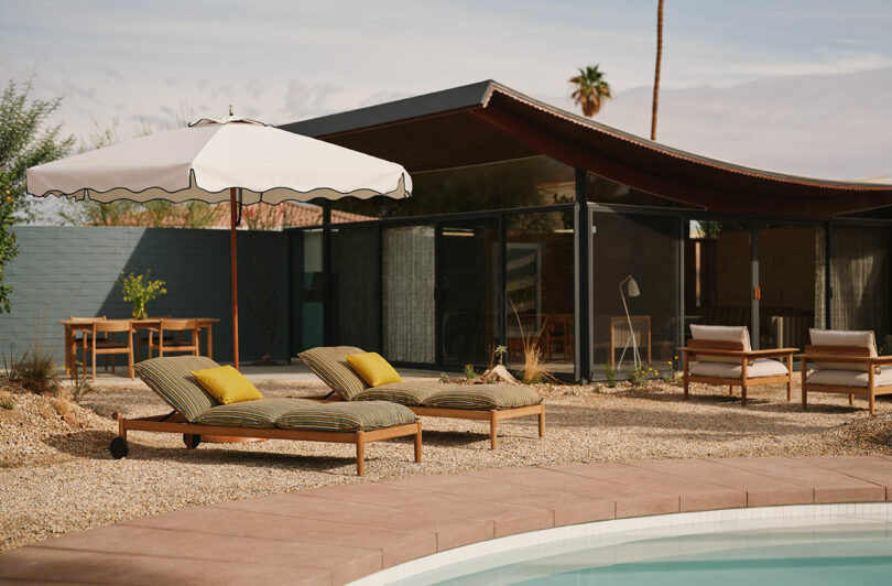 Outdoor pool area with white umbrellas and lounge chairs in a desert landscape.