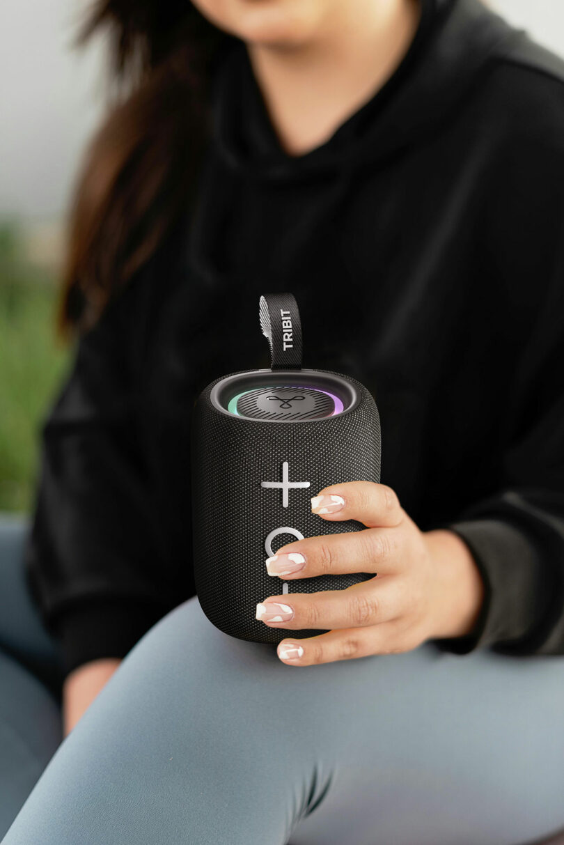 A close-up of a person holding the compact black TRIBIT StormBox Mini+ speaker, highlighting its size relative to a human hand.