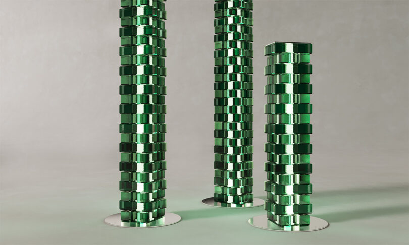 Three vertical columns made of stacked reflective green glass blocks on silver bases.