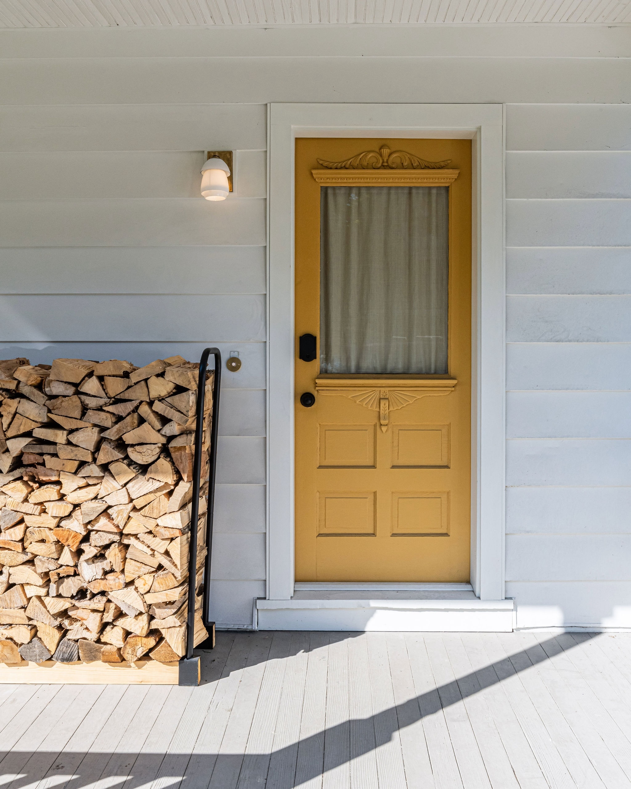 A bright India Yellow front door with a brass and milk glass sconce on a white exterior wall.