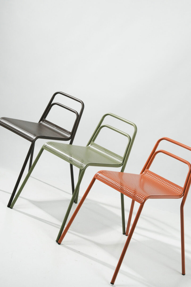Three stackable metal chairs in black, green, and terracotta orange arranged in a row.