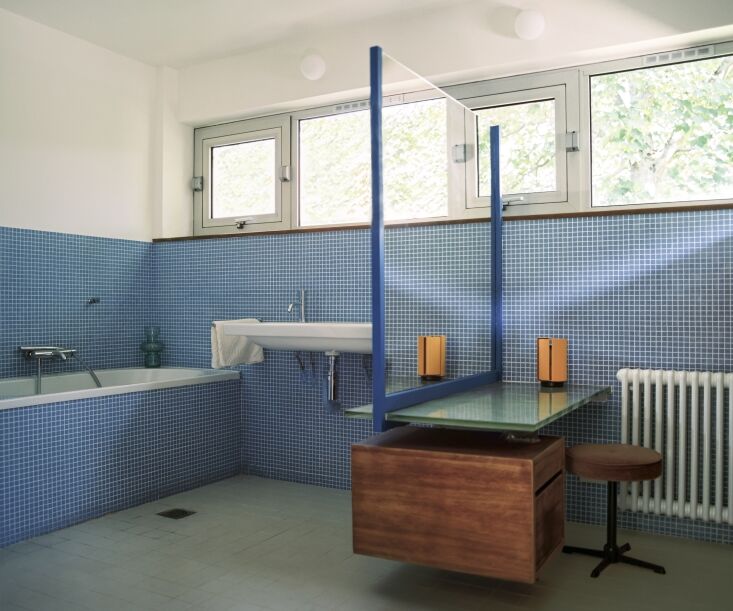 A bathroom featuring original blue tiles and an orange Charlotte Perriand Pivotante À Poser table lamp.