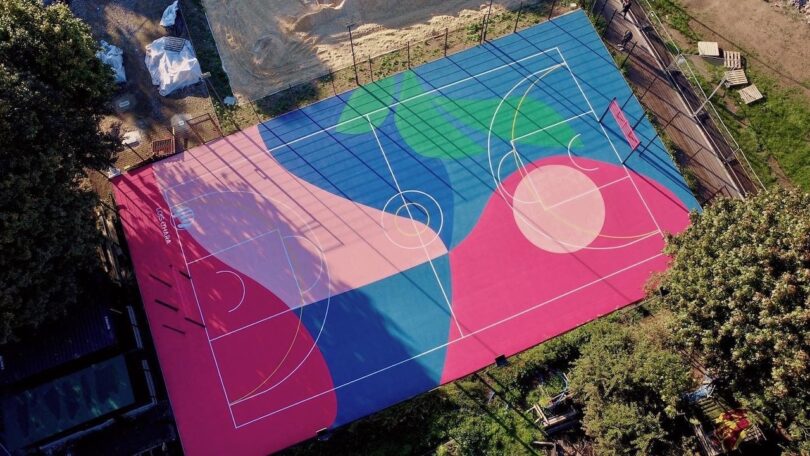 Aerial view of a basketball court painted with abstract blue, pink, and green geometric shapes.