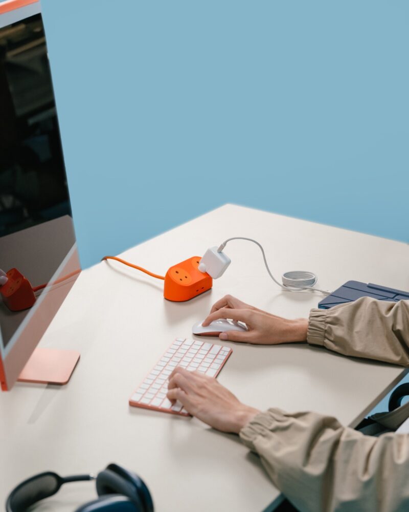 A workspace featuring a desktop computer, keyboard, mouse, and a bright orange DailyObjects power hub.
