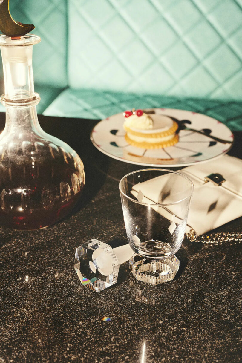 A crystal bottle stopper and decanter on a glossy table next to a luxury handbag.