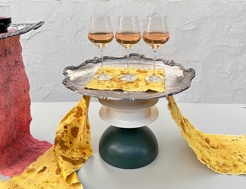 Three glasses of rosé wine on a silver tray, accented by yellow textured paper and a green-and-white pedestal.