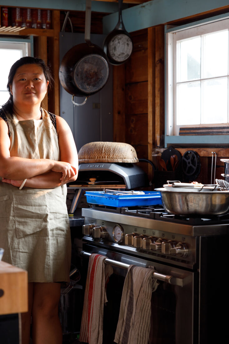 A woman cooking a lobster dish at a stove in a bright summer kitchen.