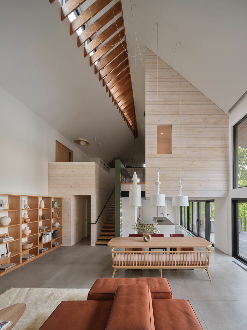 Modern open-concept living area with high ceilings, large windows, and a staircase leading to a loft.