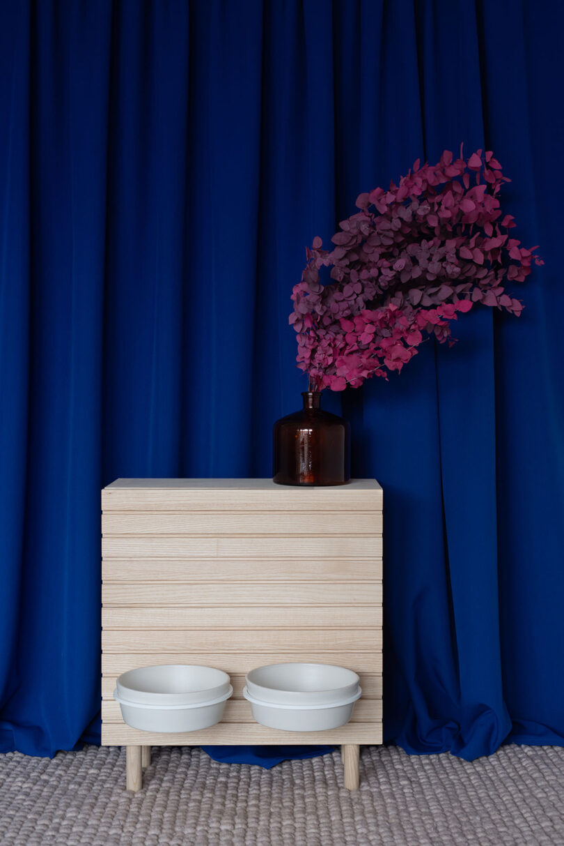 A stylish wooden cabinet with pet bowls built into the lower shelf, decorated with a vase and pink foliage.