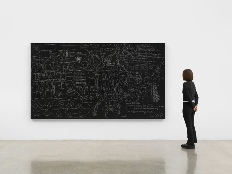 A viewer standing in front of a massive black square artwork featuring white linear diagrams resembling a complex flowchart.