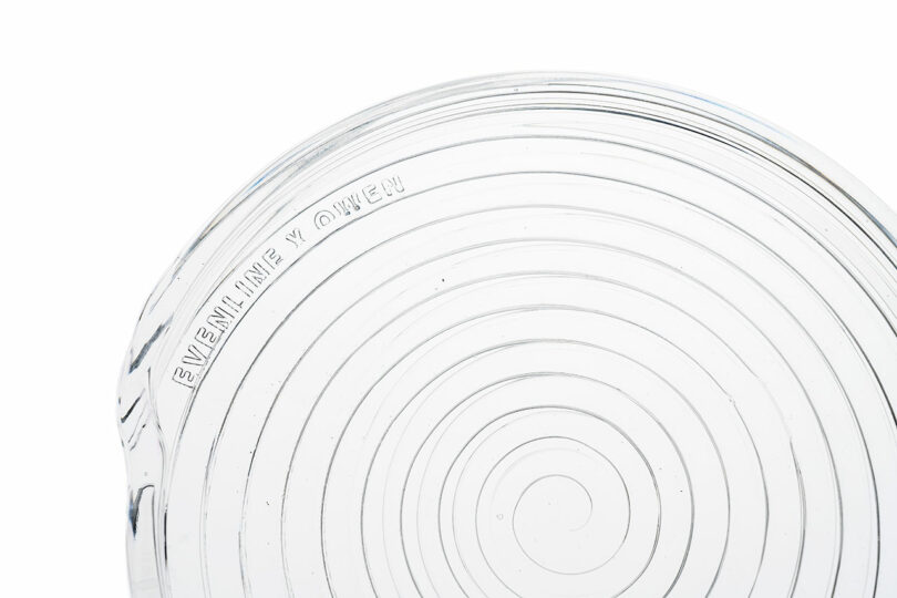 Macro close-up of a clear glass rim with concentric ridges and embossed text 'EVENLINE Y QWEEK'.