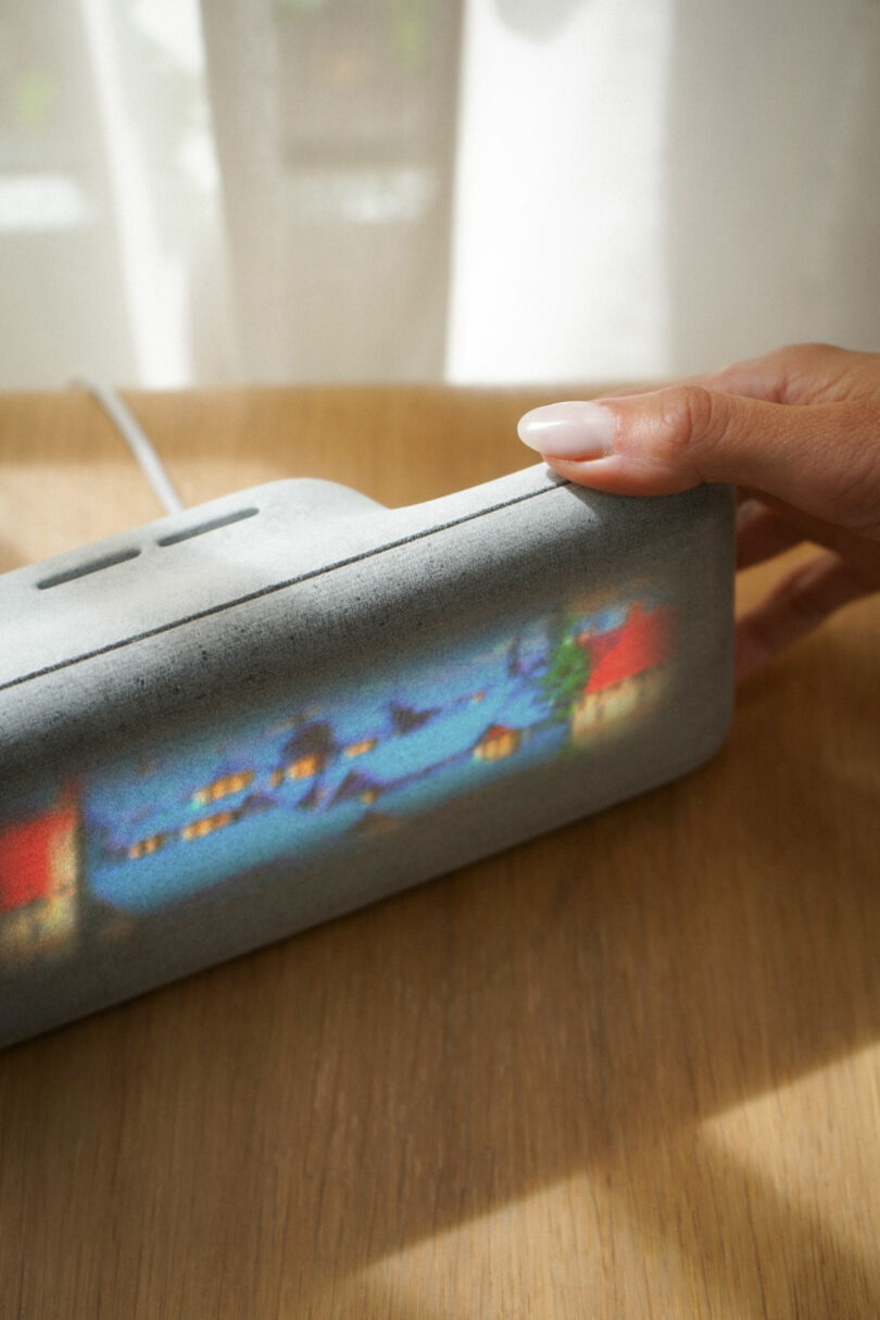 A hand adjusting a gray Dream Recorder device on a wooden surface by a window.