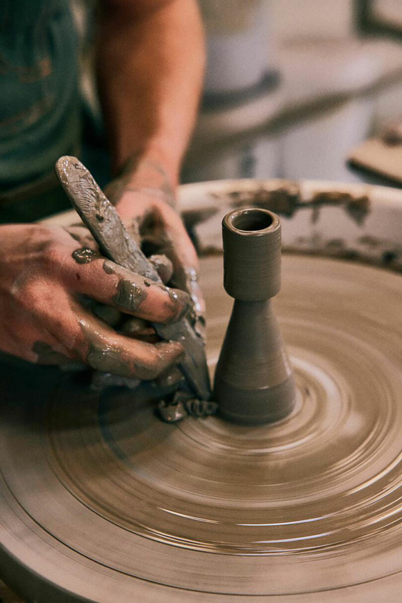 A craftsperson shaping wet clay on a pottery wheel in a minimalist studio setting.