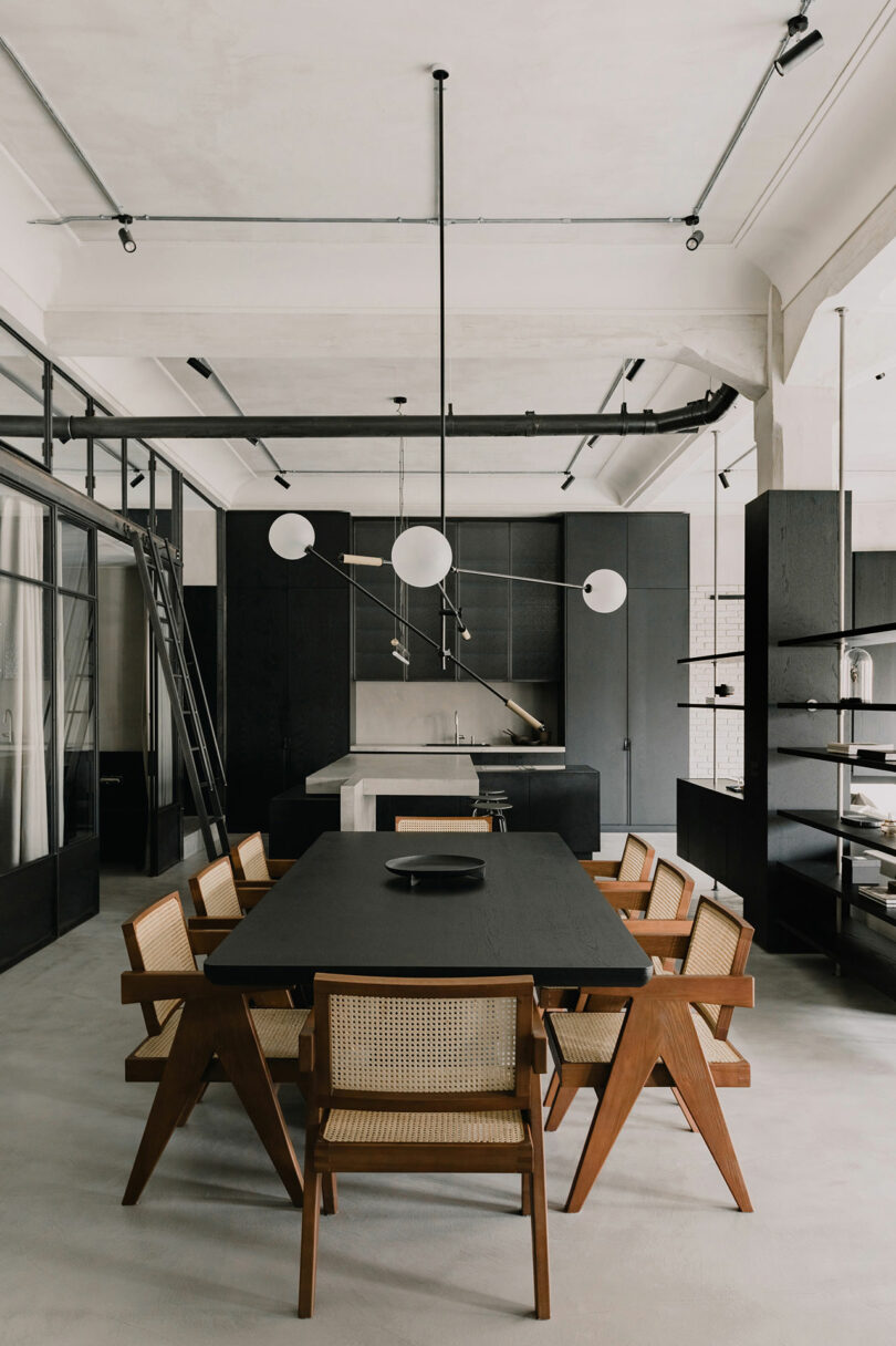 Minimalist dining room with a black table, wooden cane chairs, and modern spherical pendant lights.
