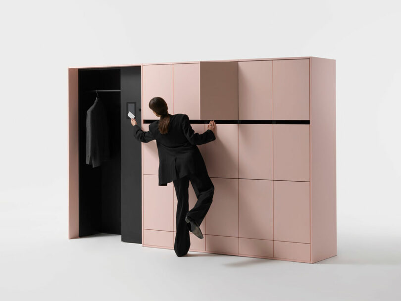 A person in professional attire standing next to a large, minimalist pink storage unit with multiple compartments.