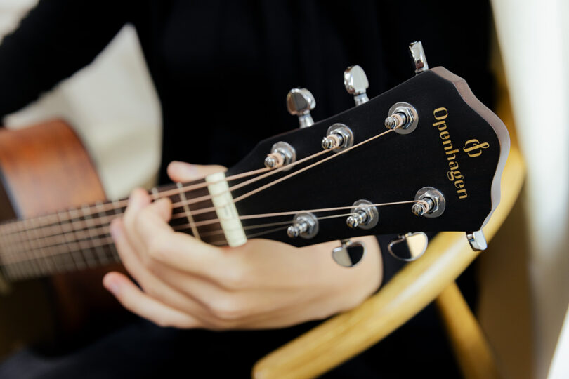 Close-up of the Openhagen brand name on the headstock of a wooden acoustic guitar.