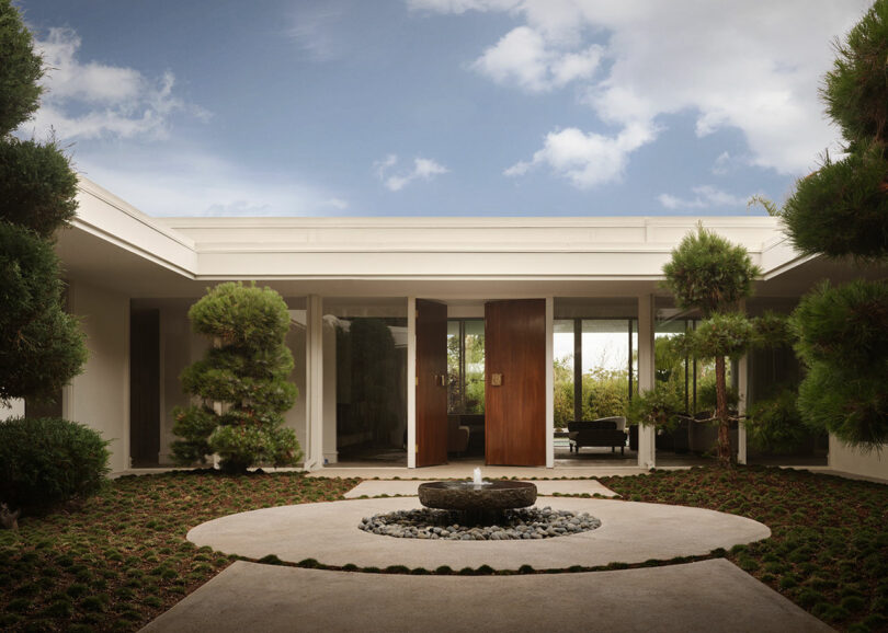 A modern courtyard with a circular stone fountain and minimalist landscaping under a clear sky.