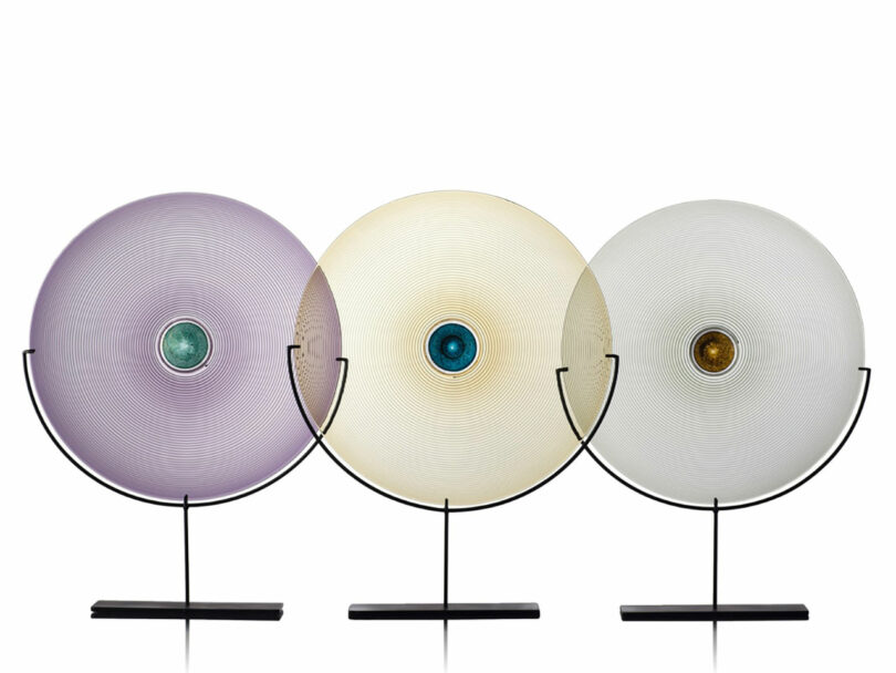 Three circular glass sculptures with colored centers on black bases.