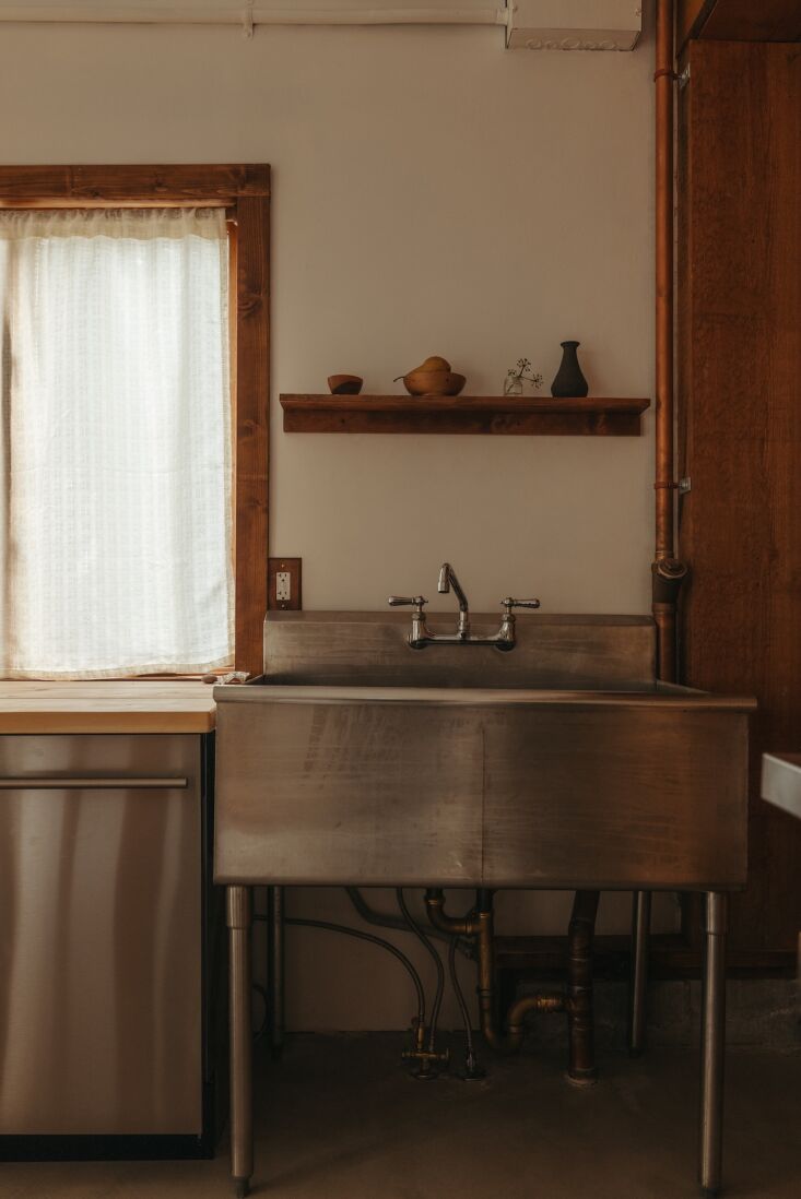 Detail of an industrial stainless steel sink with exposed copper plumbing and surface-mounted electrical boxes.