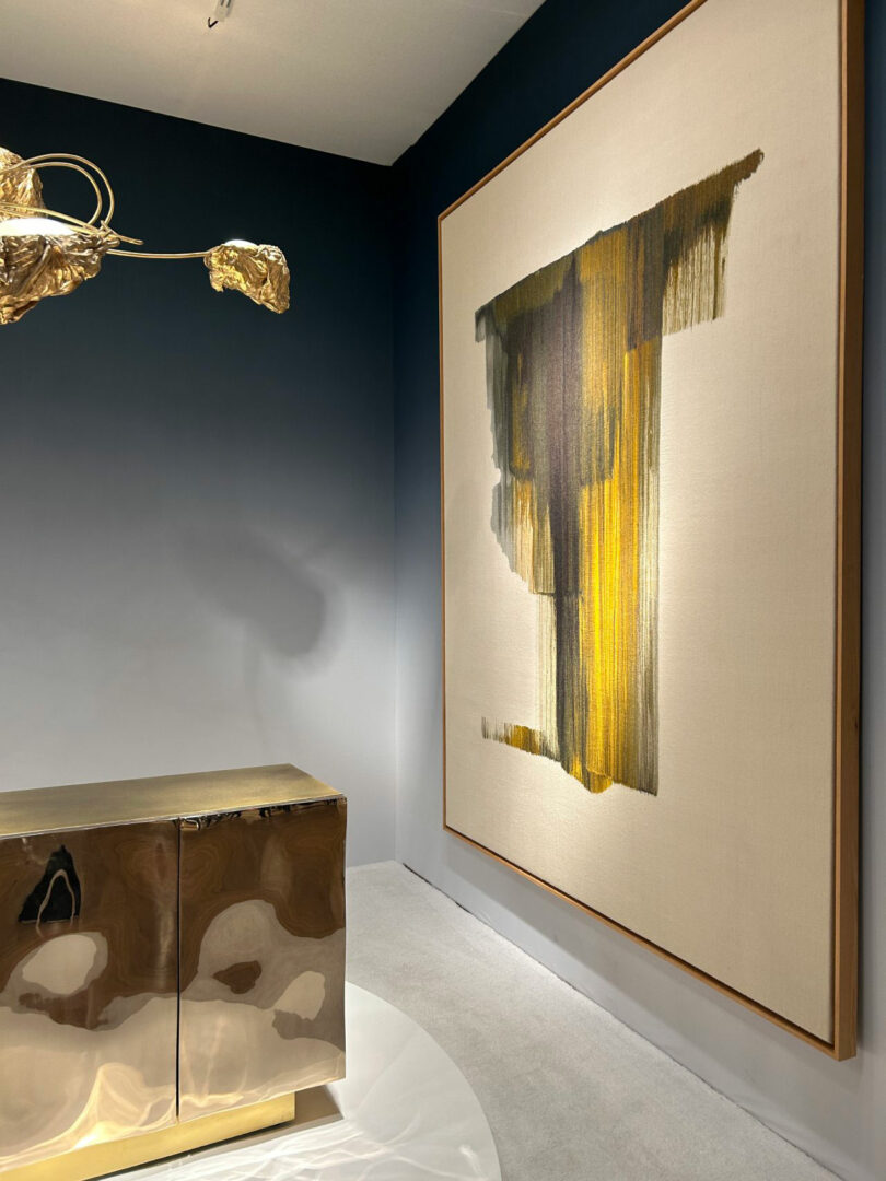 Abstract vertical streak painting hung above a metallic cabinet with a golden leaf sculpture.