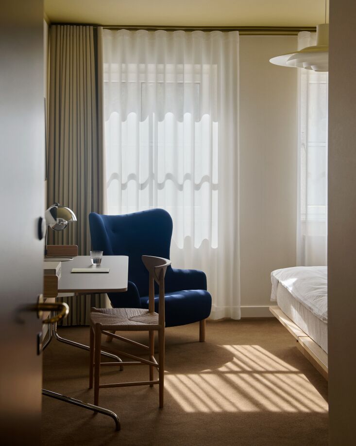 Interior of a guest room featuring a custom blue upholstered Petra Lounge Chair and soft natural lighting.