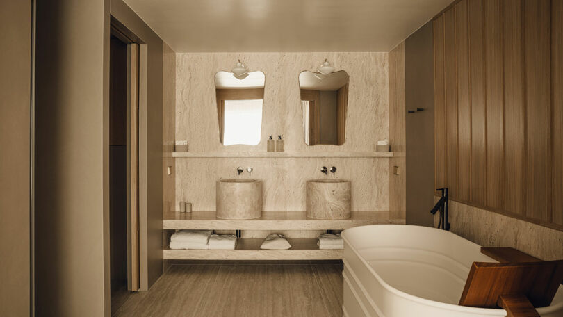 Modern bathroom at Puro Hotel with double stone sinks, wooden paneling, and a freestanding bathtub.