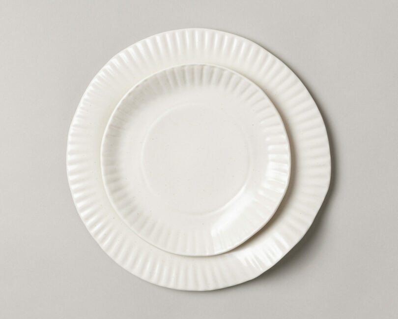 Two white ceramic plates with fluted edges stacked against a gray background.