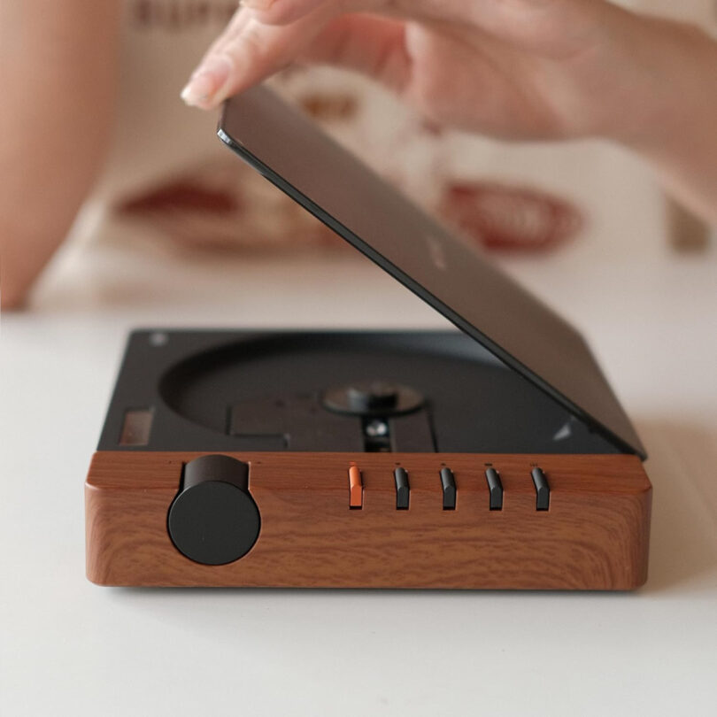 A person's hand interacting with a wood-finish CD player featuring physical buttons.