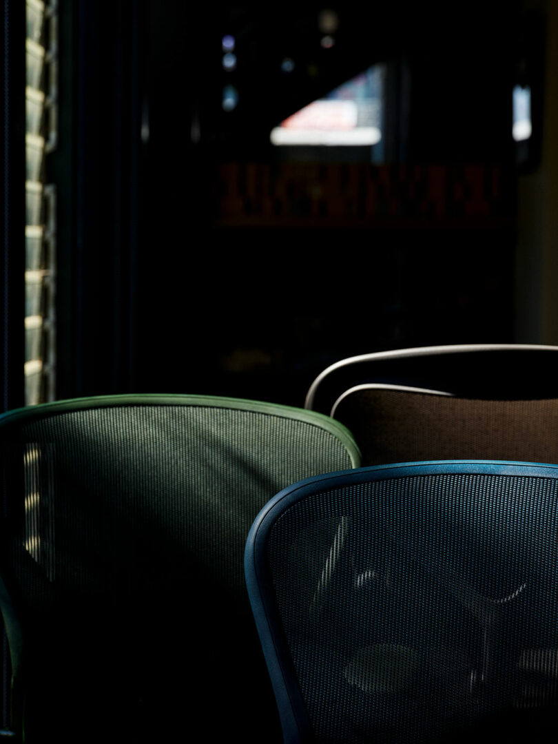 Three different colored mesh office chairs lined up against a dark background.