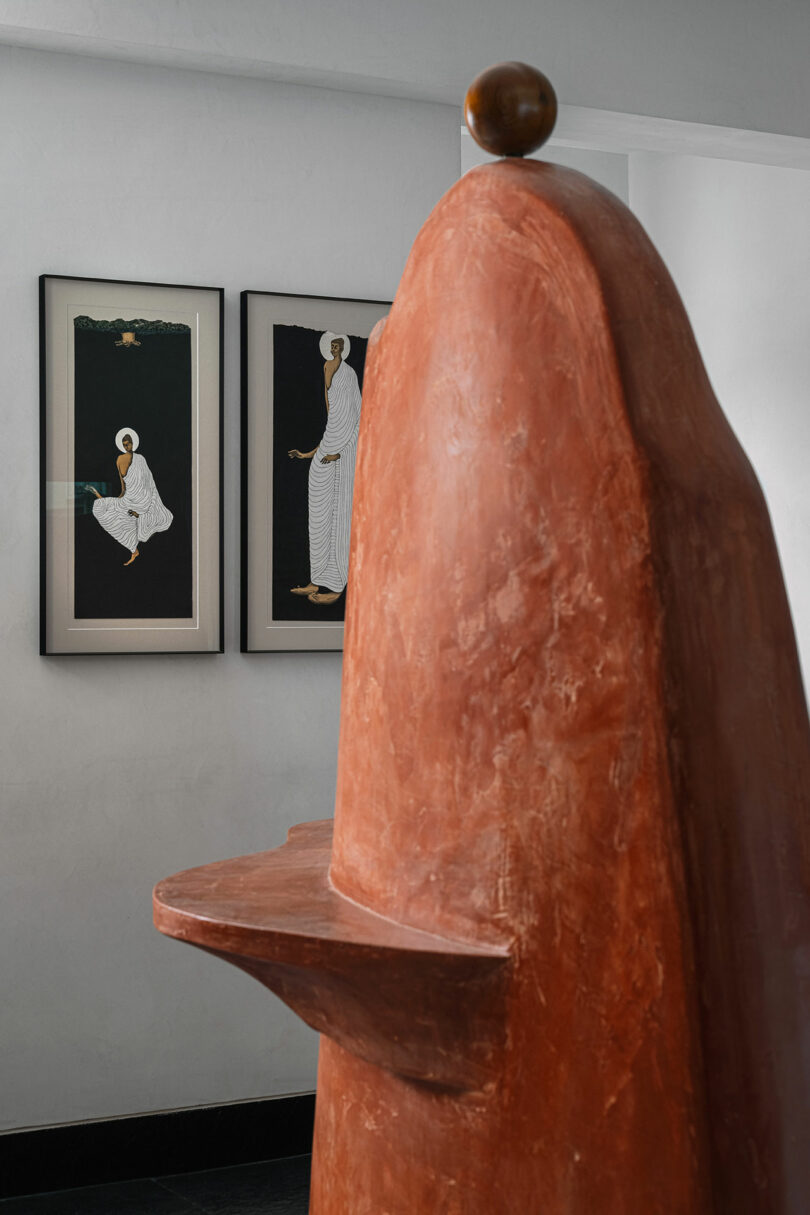 A large abstract terracotta sculpture placed in front of two framed monochromatic art pieces.