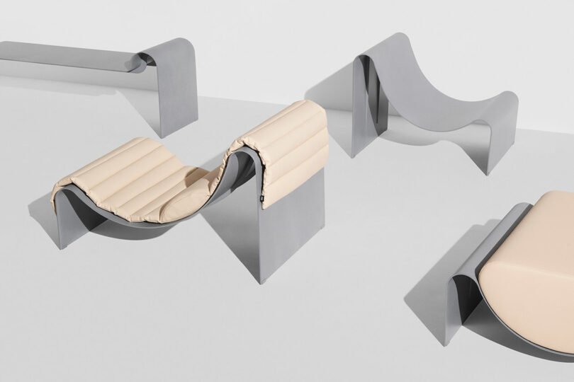 Minimalist modern furniture with curved gray metal bases and light beige cushions on a white background.