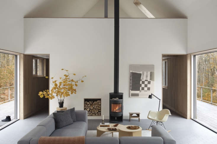 A long, narrow modern living room with a wood-burning stove and minimalist seating.