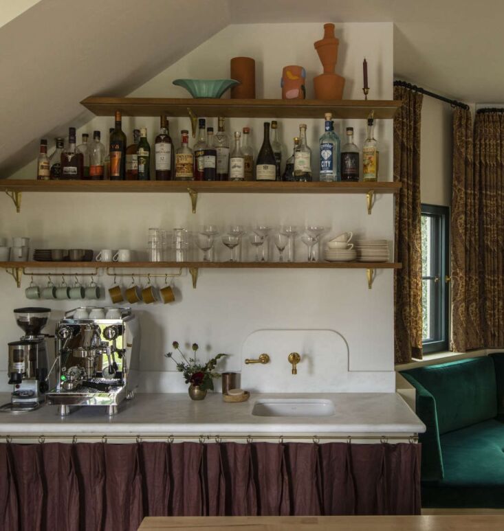 A small bar sink with a pleated plum linen skirt and a curved marble backsplash.