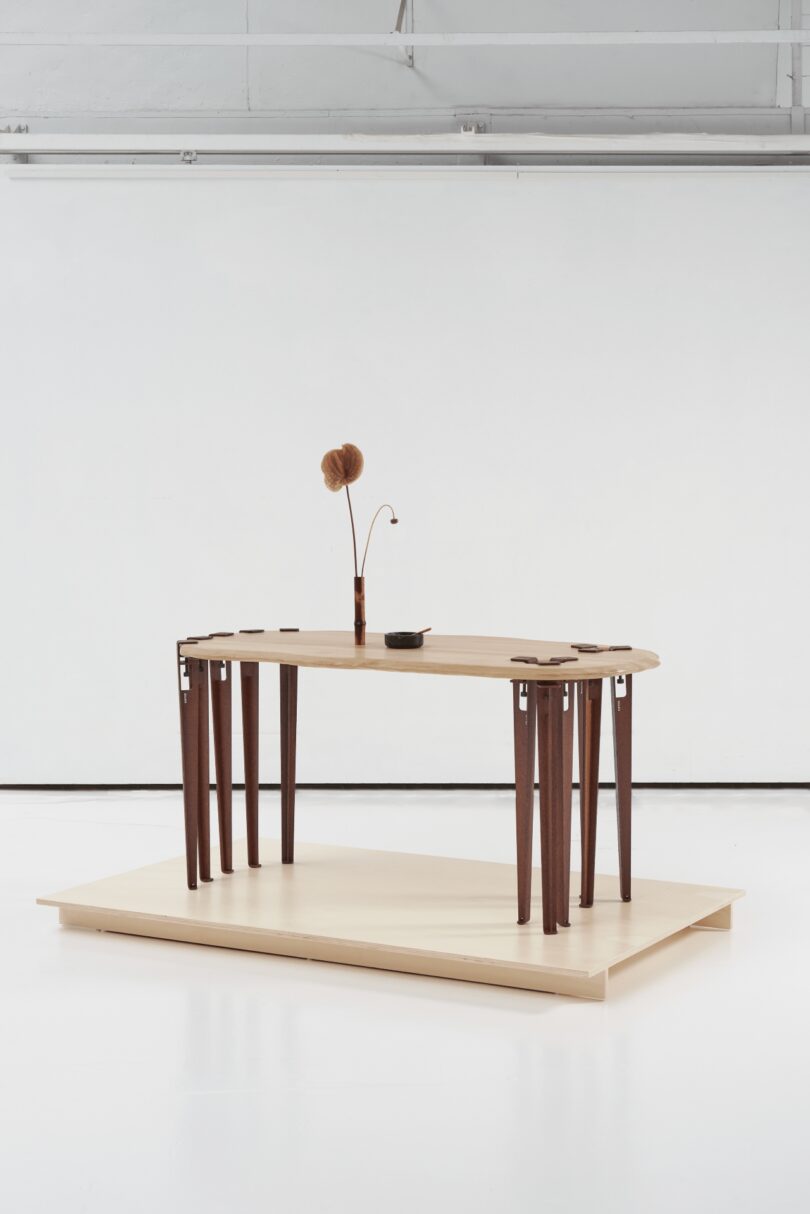 A modern wooden table with multiple dark modular legs and minimalist decor in a white industrial room.