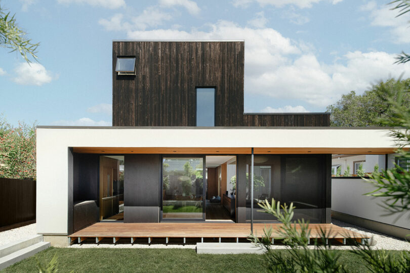 A modern two-story home with a dark wood upper level and a large covered patio area.