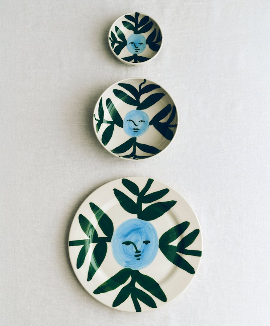 A stack of Moon Face Vine Bowls and plates featuring blue and green painted designs.