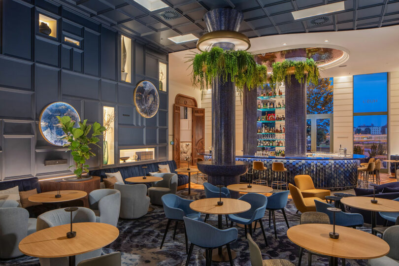 A luxurious bar area with deep blue velvet chairs and hanging plants.