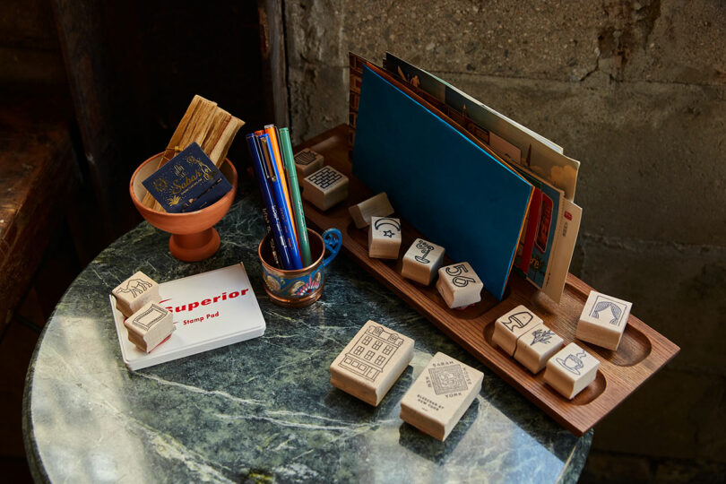 A marble table featuring wooden stamps, postcards, and colored pencils.