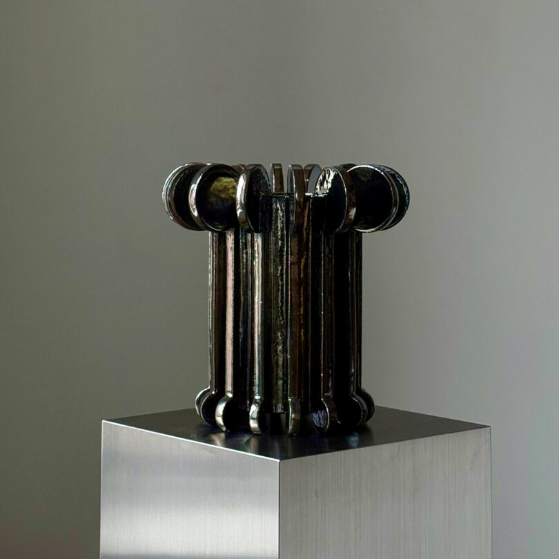 A metallic, cylindrical sculpture with rounded ends showcasing a patinated bronze-like finish.