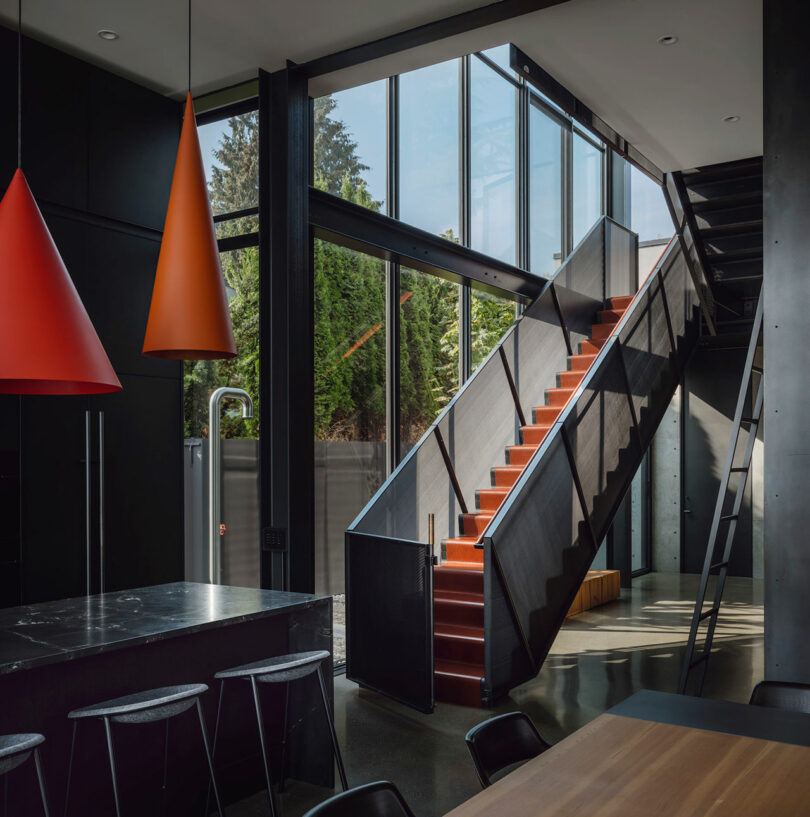 Modern interior with floor-to-ceiling windows and a sculptural black metal staircase with red steps.