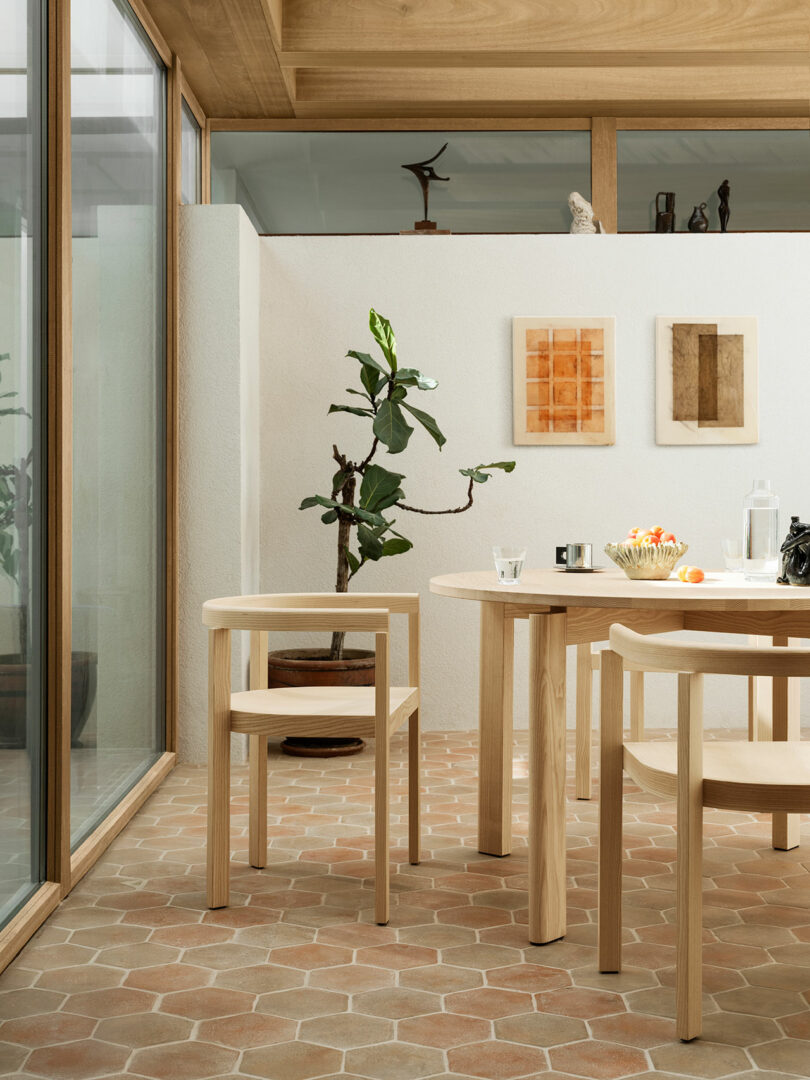 Minimalist dining area with light oak After chairs and table on a tiled floor with natural lighting.